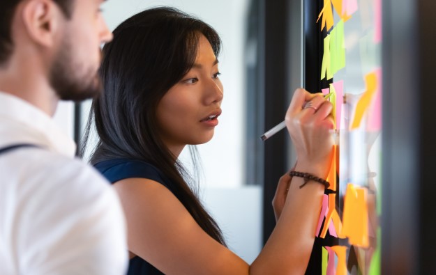 People writing on colored sticky notes affixed to a board